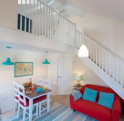 A dining area with a table and chairs next to a red sofa under a staircase at Brinyloft in Carbis Bay