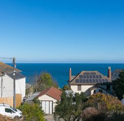 Houses with rooftops including one with solar panels and a van parked near them overlooking the ocean at Cornerways in Carbis Bay