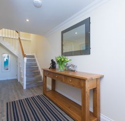 A hallway with a wooden console table holding a vase of flowers and decorative items and a mirror above it at Cornerways in Carbis Bay
