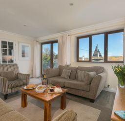 A living room with sofas a coffee table with snacks and drinks and a window with a sailboat decoration at Cornerways in Carbis Bay