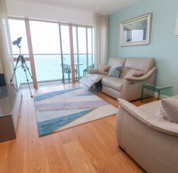 A living room with beige sofas blue rug and a telescope by glass doors with an ocean view at Elanora in Carbis Bay