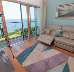 A living room with a beige recliner sofa a colorful geometric rug a telescope and a balcony overlooking the sea at Elanora in Carbis Bay