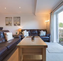 A living room with two brown leather couches a wooden coffee table and a floor lamp near a sliding glass door at Gennaker in Carbis Bay