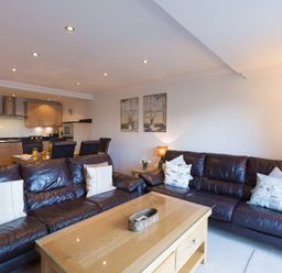 A living room with leather sofas and a wooden coffee table adjacent to a dining area and kitchen at Gennaker in Carbis Bay