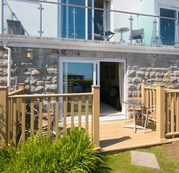 A patio with a wooden railing, metal chairs and tables outside a stone and white building at Gennaker in Carbis Bay