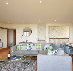 A living room with a gray sofa and patterned pillows next to a glass coffee table and dining table at Halcyon Cove in Carbis Bay