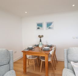 A dining table set with plates bowls glasses and a vase with flowers in a room with two grey chairs at Kernow's Dream in Carbis Bay