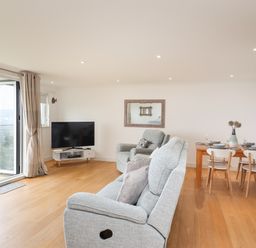 A living room with grey upholstered chairs a wooden dining table with chairs and a television at Kernow's Dream in Carbis Bay