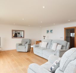 A living room with gray upholstered armchairs and sofa a TV on a stand and a wooden floor at Kernow's Dream in Carbis Bay