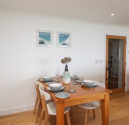 A dining area with a wooden table set for four with plates glasses and a vase with flowers at Kernow's Dream in Carbis Bay