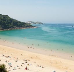 A beach with people on sand and in water near a green hillside at Ocean Cove in Carbis Bay