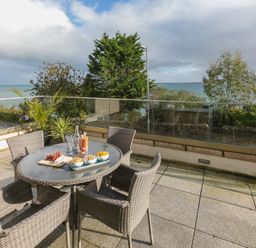 An outdoor patio with a round glass table and four wicker chairs overlooking the sea at The View in St Ives