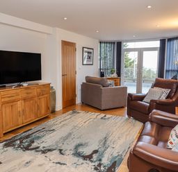 A living room with a wooden cabinet and television a gray armchair and brown leather sofas next to glass doors at The View in St Ives