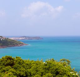 A coastal view with green shrubs in the foreground blue sea and a headland with buildings at Portside in Carbis Bay