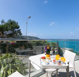 A balcony with a small table set with drinks and snacks overlooking the sea at Portside in Carbis Bay