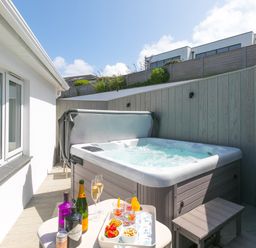 An outdoor patio with a hot tub a small table with drinks and snacks and wooden fencing at Portside in Carbis Bay