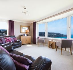 A living room with leather sofas armchairs a wooden cabinet and large windows overlooking the sea at Seathrift in Carbis Bay