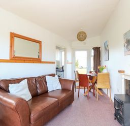 A living room with a brown leather sofa two white pillows a dining table with four chairs flowers on the table a small stove a mirror on the wall and a door at the back at Chalet 150 in Winterton-On-Sea