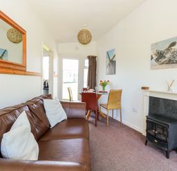 A living room with a brown leather sofa white cushions a small dining table with chairs flowers and pictures on the walls at Chalet 150 Winterton-On-Sea