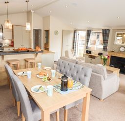 An open plan living room and kitchen with dining table set for breakfast and sofas near a fireplace at Seagull Lodge in Runswick Bay