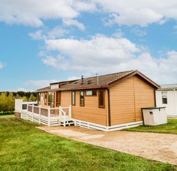 A wooden lodge with a white railing and steps on a paved pathway surrounded by grass at Woodland View Lodge Swarland near Felton