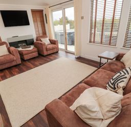 A living room with brown sofas chairs a beige rug and a wall mounted television at Woodland View Lodge Swarland near Felton