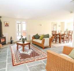A living room with wood stove tv and wicker sofas and a dining area at The Hermitage in West Beckham near Sheringham