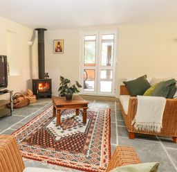 A living room with a wood stove fire a patterned rug a wooden coffee table wicker furniture and a television at The Hermitage in West Beckham near Sheringham