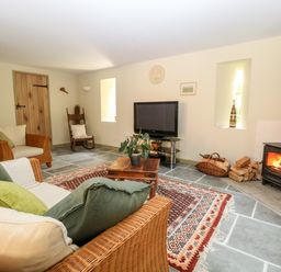 A living room with sofas a wooden coffee table a television and a wood burning stove at The Hermitage West Beckham near Sheringham