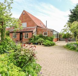 A brick house with a tiled roof and garden with plants and trees at The Hermitage in West Beckham near Sheringham