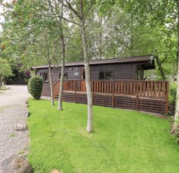 A cabin with a deck surrounded by grass and trees at Squirrels Leap, Number 29, Burnside Park near Keswick