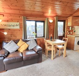 A living room with a sofa, dining table, and kitchen unit at Squirrels Leap, Number 29, Burnside Park near Keswick