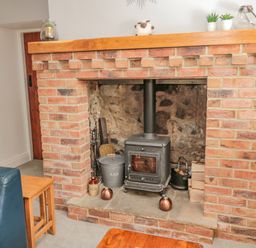 A wood burning stove inside a brick fireplace with wood logs and ash bucket in a living room at Woolley Lodge in Wooler