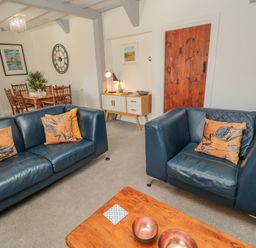 A living room with blue leather sofas and orange cushions a wooden coffee table with bowls a dining table with chairs and a wall clock and sideboard at Woolley Lodge in Wooler