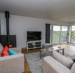 A living room with sofas a TV a wood burner and large glass doors leading to a patio and garden at Llyn Cae Ty Nant Fishery Holiday Let in Bwlchllan near Llangeitho