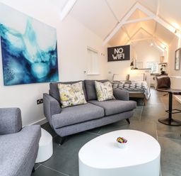 A living area with gray sofas, a white coffee table, bar stools, a bed, and a no wifi sign at Twigs in Woody Bay