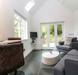 A living room with gray sofa and armchair and white round coffee table with glass door to a garden at Twigs in Woody Bay