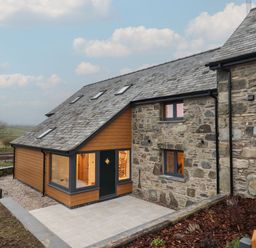 An exterior view of a stone and wood house with a slate roof and a paved patio area at Merddwr in Cerrigydrudion