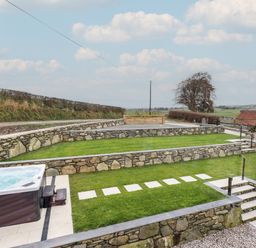 A tiered garden with stone walls and a hot tub at Merddwr in Cerrigydrudion