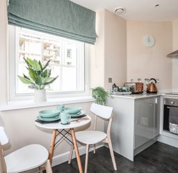 A small kitchen with a round table set for two green dishes white chairs a window with a green blind and kitchen appliances at Nantlle in Caernarfon