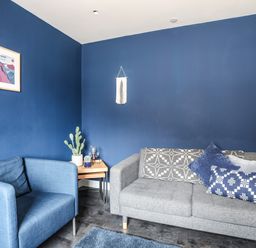 A living room with blue walls a blue armchair a grey sofa with cushions and a small wooden side table with plants at Nantlle in Caernarfon