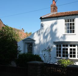 A white house with a tiled roof surrounded by bushes and a black metal gate at Phloxhaven in Reedham
