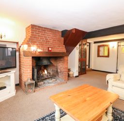 A living room with a brick fireplace a television on a white stand a wooden coffee table and an armchair at Phloxhaven in Reedham