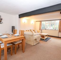 An open plan living and dining area with a wooden dining table set and beige sofas near a window at Phloxhaven in Reedham