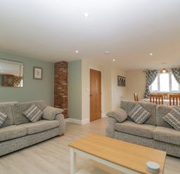 A living room area with two grey sofas and a wooden coffee table next to a dining table with wooden chairs and window at Bramley Cottage Henley near Langport