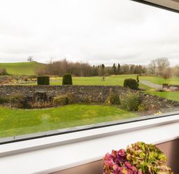 A view of a garden with a stone wall and greenery outside a window at Carus House at Carus Green Golf Club in Kendal