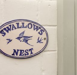An oval sign with illustrations of swallows and the text Swallows Nest on a white painted brick wall at Swallows Nest in Whitby