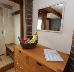 A hallway with a wooden cabinet holding a basket of snacks and a book beside a brick pillar and a mirror at Swallows Nest Whitby