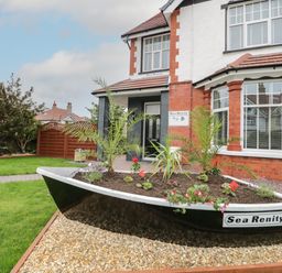 A boat-shaped garden planter with plants and flowers in front of a brick and white two-story house at 23 Carmen Sylva Road in Llandudno