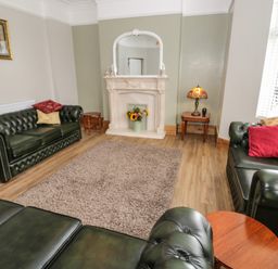 A living room with green leather sofas a fireplace flower vase and a window at 23 Carmen Sylva Road in Llandudno